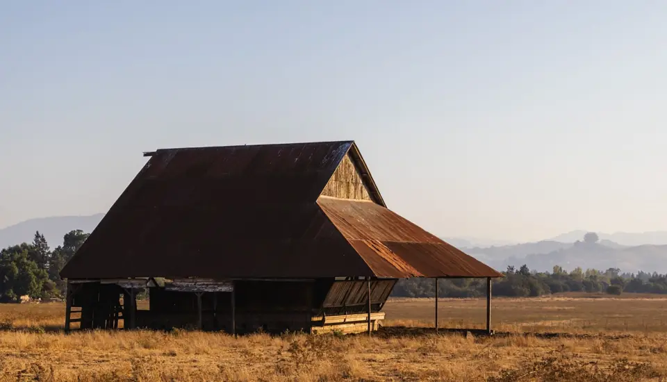 Barn with a rusted metal roof on open farmland at sunset