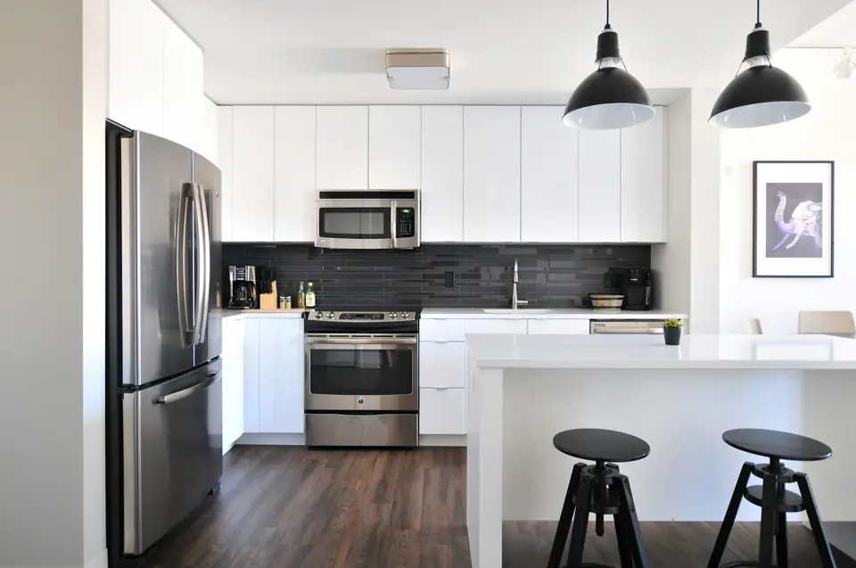 White kitchen with black pendant lights, stainless appliances and an island with two stools