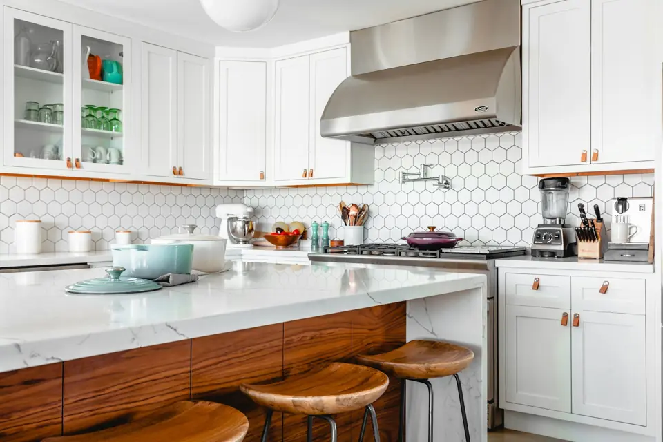 White kitchen with a stainless range hood, hexagon tile backsplash and wood bar stools