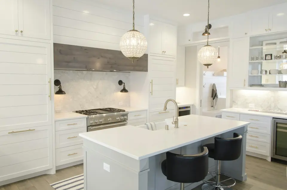 White kitchen with a large island, marble counters and black bar stools