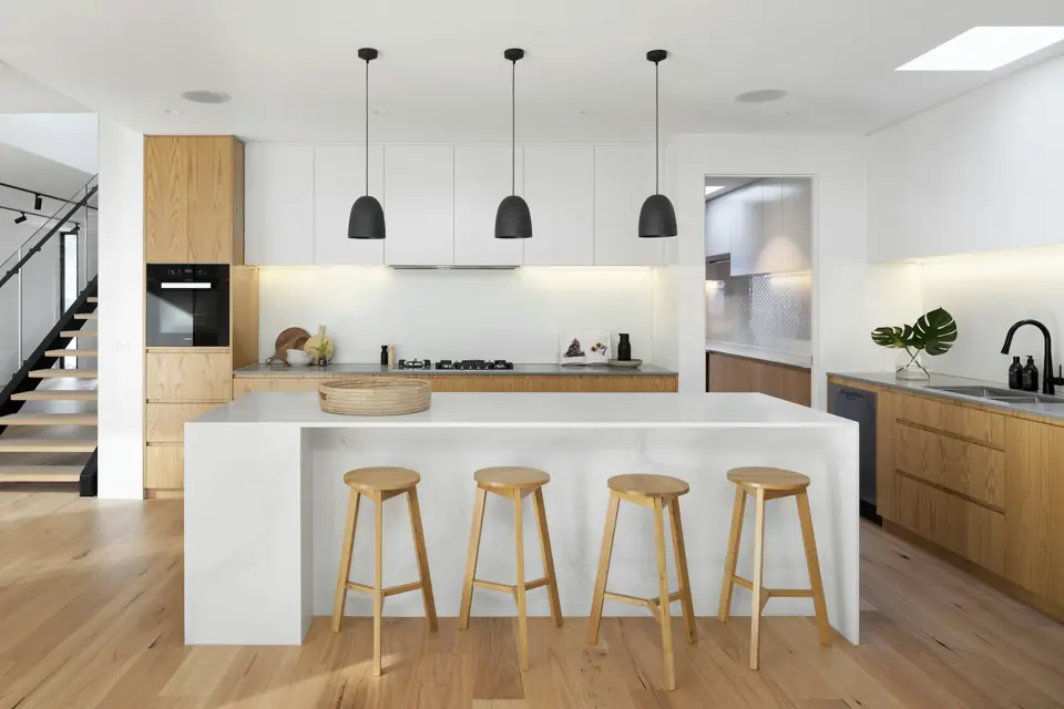Bright kitchen with white counters, wood cabinets and wooden bar stools at the island