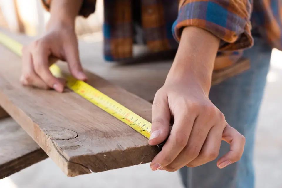 Hands measuring a wood board with a tape measure