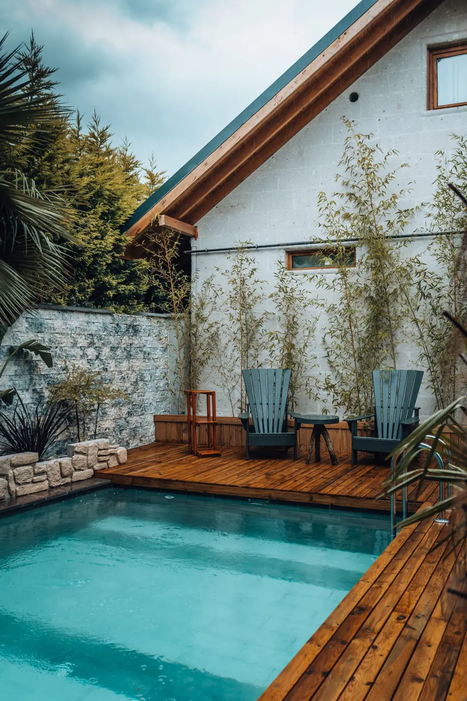 Small white pool house beside a pool with a wood deck