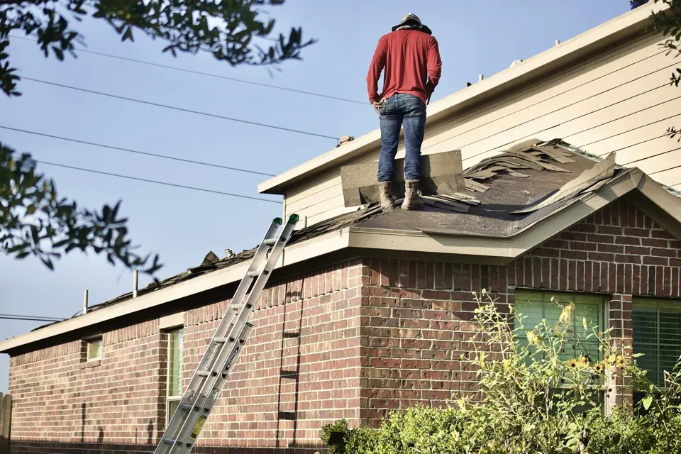Roofer standing on the roof of a brick house next to a ladder